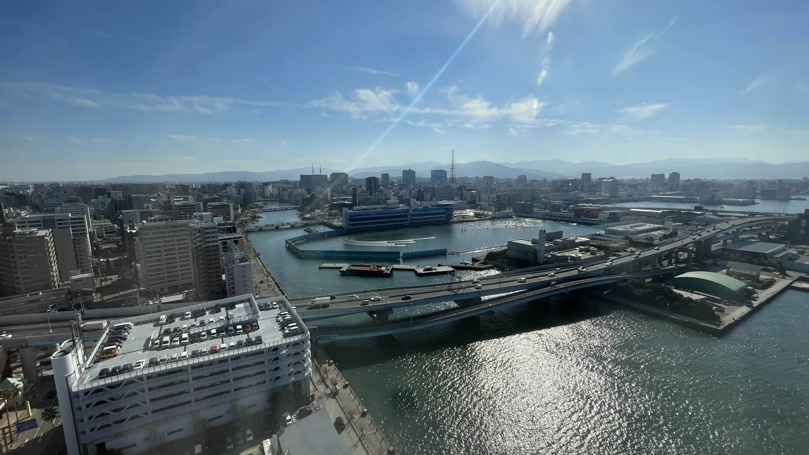 博多ポートタワーからの博多の景色の写真。晴天と市街地、海とその上にあるボートレース場が映っている。